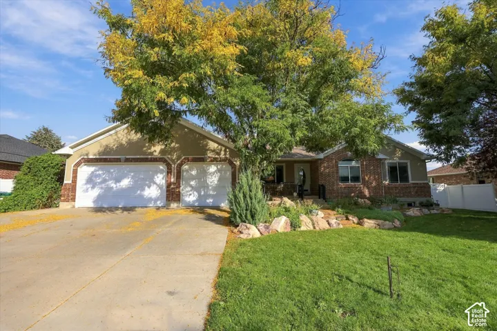 Exterior featuring a two-car garage, brick facade accents, and a landscaped front yard with mature trees
