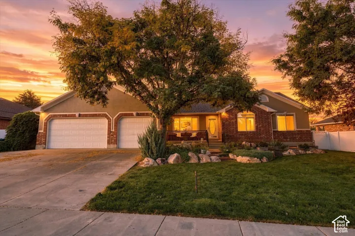 Brick single-story residence with dual-car garage, illuminated by warm interior lighting at dusk