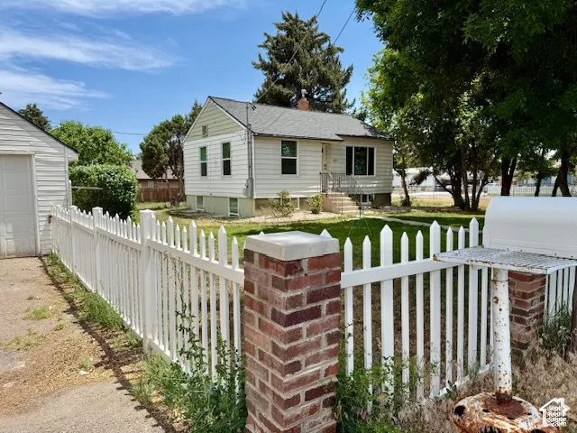 White picket fence with brick pillars, a detached garage, and a manicured lawn