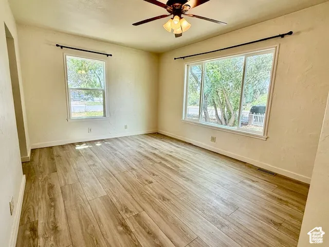 Wood-finish flooring, ceiling fan with integrated lighting, and multiple windows providing natural illumination