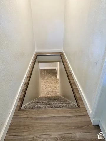 Wood-finish flooring with crisp white baseboards, textured white walls, and a carpeted staircase