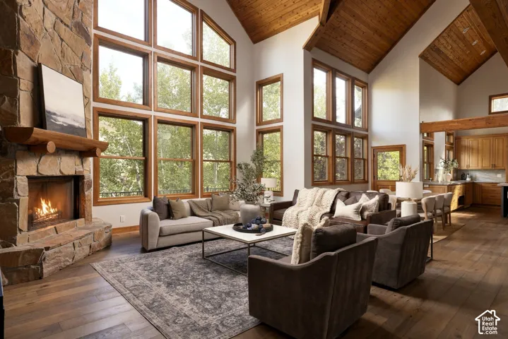 Stacked stone fireplace with a substantial wood mantel, extensive wood-framed windows, vaulted wood-paneled ceilings, wood-finish flooring, and exposed wood beams