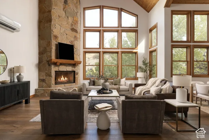 Vaulted wood-paneled ceiling, stone-clad fireplace with a solid wood mantel, full-height windows, wood-finish flooring, and a built-in air conditioning unit