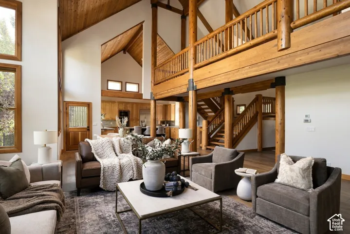 Expansive living area featuring soaring vaulted ceilings, exposed timber beams, a second-story interior balcony, and wood-finish flooring