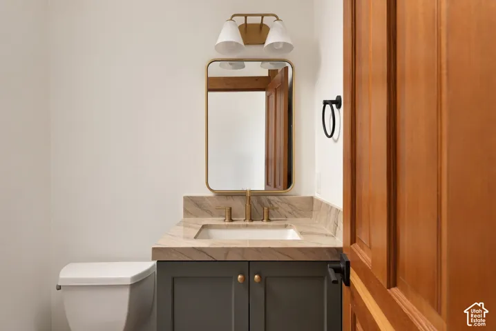 Elegant half bath featuring a dark cabinetry vanity with brass hardware, warm wood-finish framing around the mirror, and a marble-look countertop with integrated sink