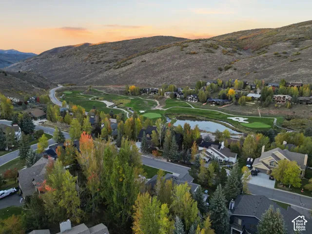 Expansive golf course property featuring mature trees and a tranquil pond, nestled against a mountainous backdrop
