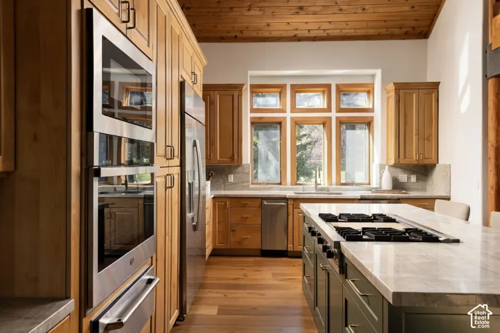 Custom wood cabinetry, stainless steel appliances, wood-finish flooring, natural wood ceiling, and an expansive island with a built-in cooktop