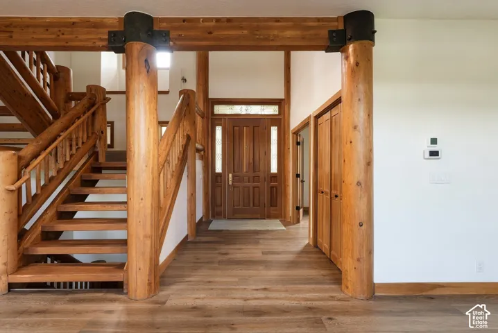 Grand entry featuring a solid wood door with sidelights, wood-finish flooring, and a prominent wood staircase with log newel posts