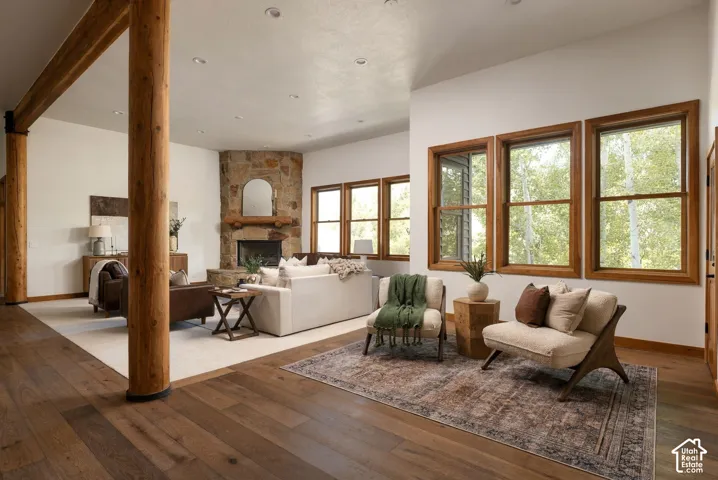 Hardwood flooring throughout, exposed timber support beams, stone fireplace with a wood mantle, and multiple windows with wood trim