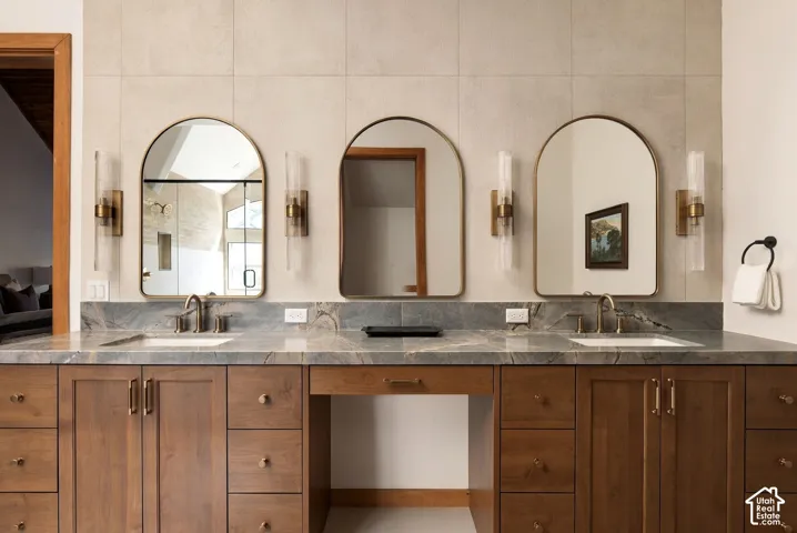 Double vanity with integrated sinks, wood-finish cabinetry, stone countertop, and three arched mirrors