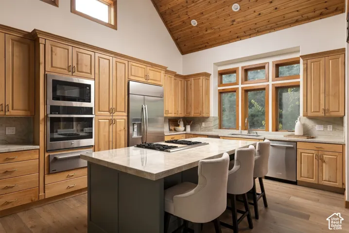 Vaulted wood-paneled ceiling, wood-finish flooring, custom wood cabinetry, stainless steel appliances, and a central island with cooktop