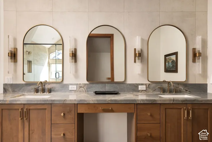 Spa-inspired dual-vanity bathroom showcasing three arched mirrors with brass-finished sconces, warm wood cabinetry with integrated hardware, and a gray-veined stone countertop