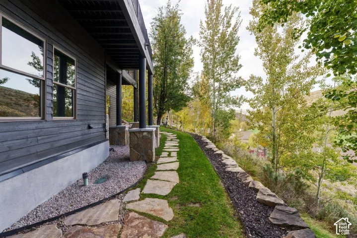 Exterior featuring dark horizontal siding, stone-clad foundational pillars, a stone paver pathway, and a landscaped terraced hillside
