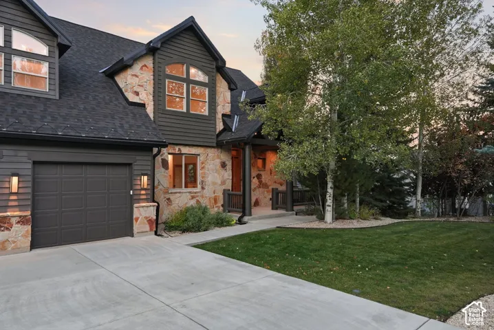 Stone and siding exterior with a multi-pane arched window, dark asphalt shingle roof, and an attached garage with carriage-style lighting