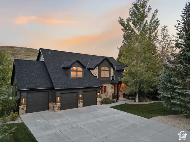 Exterior featuring dark siding, stone accents, multiple dormer windows, a three-car garage, and a concrete driveway