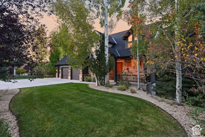 Elegant residence set on manicured grounds featuring a sweeping lawn bordered by mature birch and evergreen trees, gravel hardscaping, and a curved driveway approach