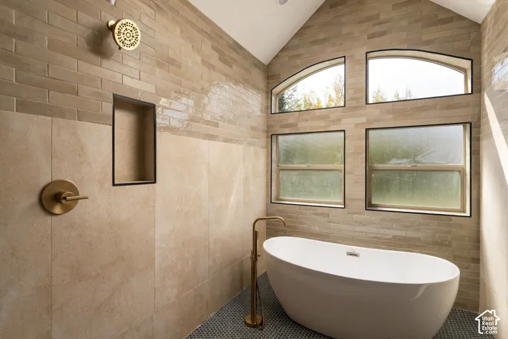 Spa-inspired primary bath featuring a freestanding soaking tub with integrated deck-mount faucet, linear tile flooring in charcoal and neutral tones, stacked tile walls in warm earth tones, recessed niche shelving, and expansive transom windows with arche