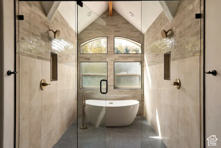 Dual walk-in showers with brass fixtures, freestanding bathtub, arched windows, and tile flooring