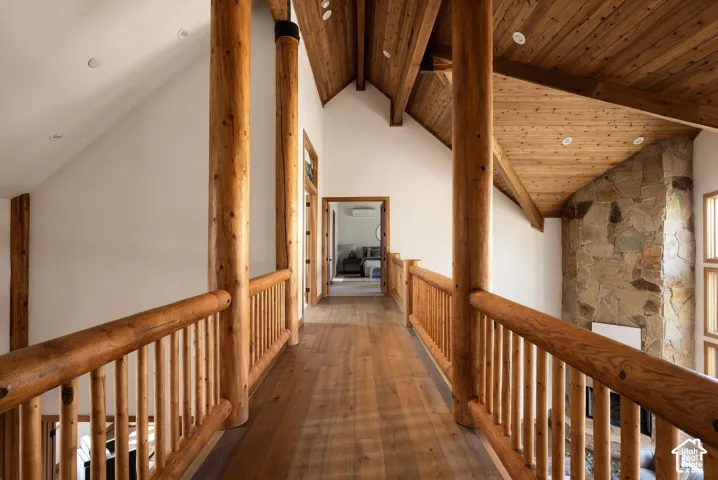 Wood-finish flooring, log beam railing, vaulted wood-paneled ceiling, stone fireplace, and recessed lighting