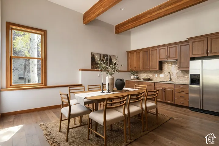 Vaulted ceilings with exposed wood beams, wood-finish flooring, wood cabinetry, granite-style countertops, and a tiled backsplash
