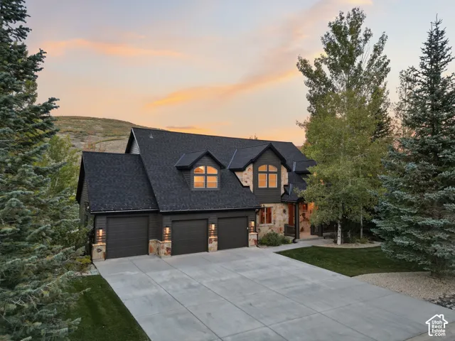 Multi-gable roofline, stone and siding exterior, triple garage doors, concrete driveway, and mature landscaping