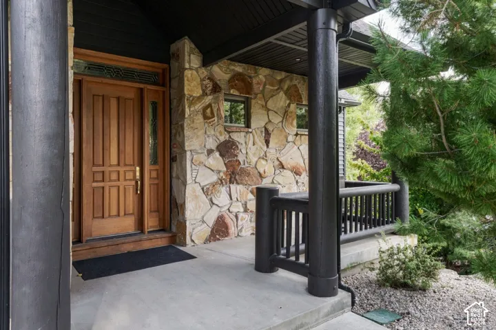 Crafted wood entry door with transom and sidelight, natural stone facade, concrete porch, and black-finished railing