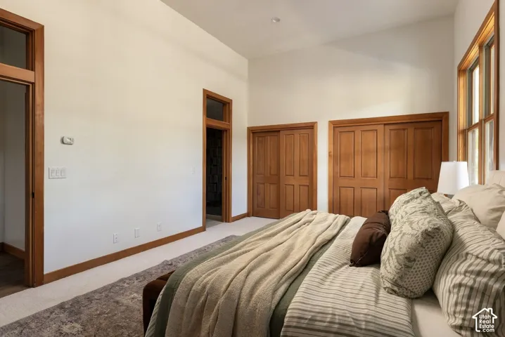 Vaulted ceiling, two sets of wooden bi-fold closet doors, wood-trimmed windows, wood door frames, and carpeted flooring