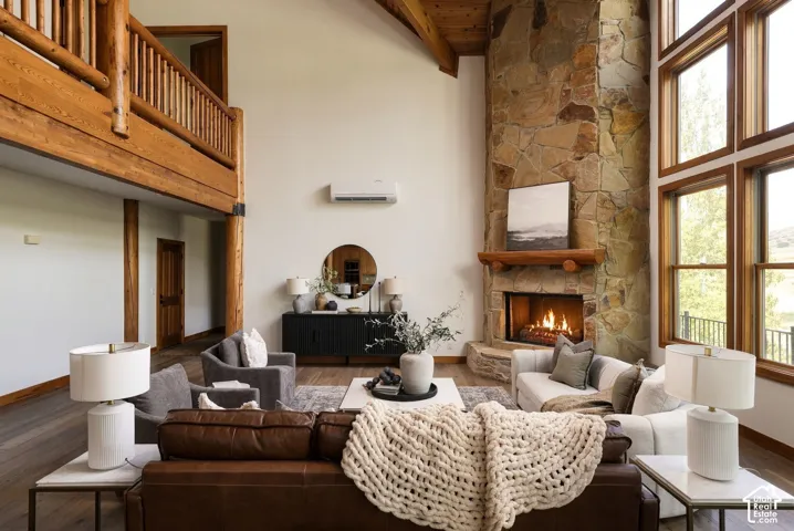 Vaulted ceiling with wood beams, stone fireplace, wood-finish flooring, and a second-story landing with wood railing