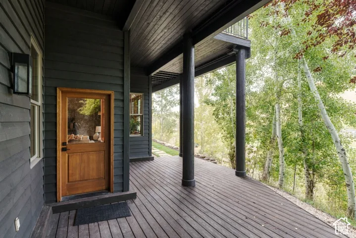 Covered wraparound deck with composite decking and support columns overlooking wooded landscape