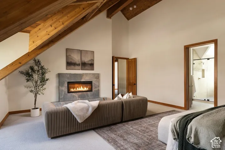 Vaulted ceiling with exposed wood beams, fireplace with stone surround, and light-colored carpeting