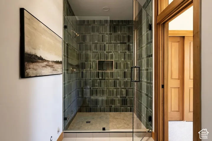 Walk-in shower with dark green subway tile, built-in shower niche, glass enclosure, and black hardware