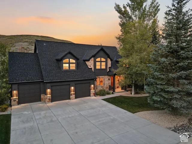 Stone and siding exterior with a dark shingle roof, featuring a three-car garage and dormer windows