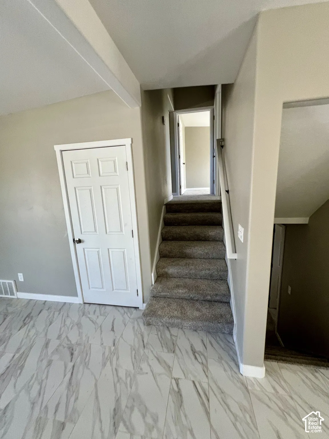 Marbled-finish floor tiles, carpeted staircase with white risers, and a white six-panel interior door