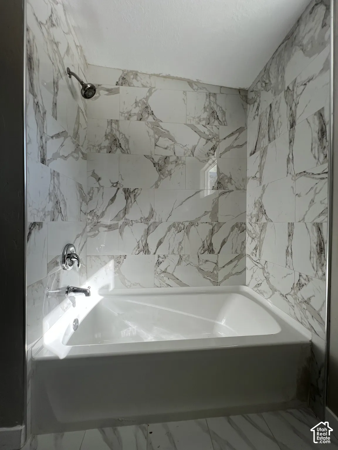 Bathtub shower combination with white and gray patterned tile surround, chrome shower head, and matching chrome fixtures