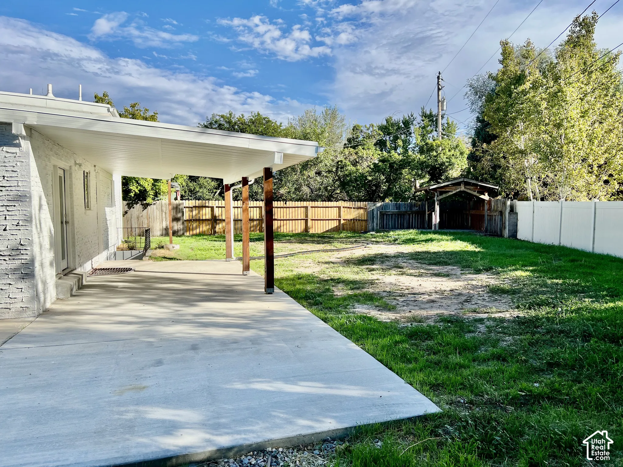 Expansive outdoor patio with a covered area, supported by wood posts, leading to a large grass yard