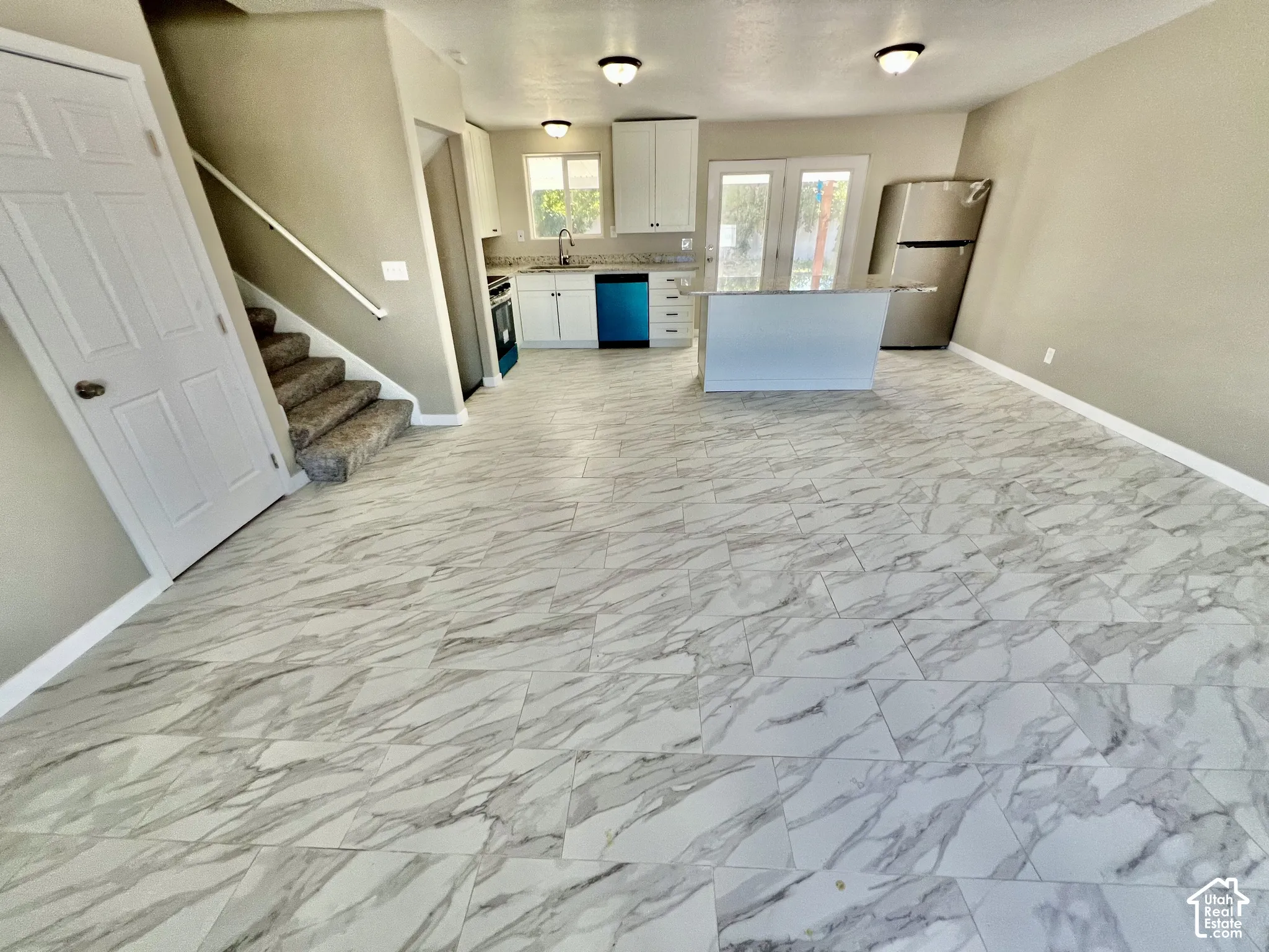 Open-concept living space with large format tile flooring, a kitchen island, stainless steel refrigerator, and dual French doors