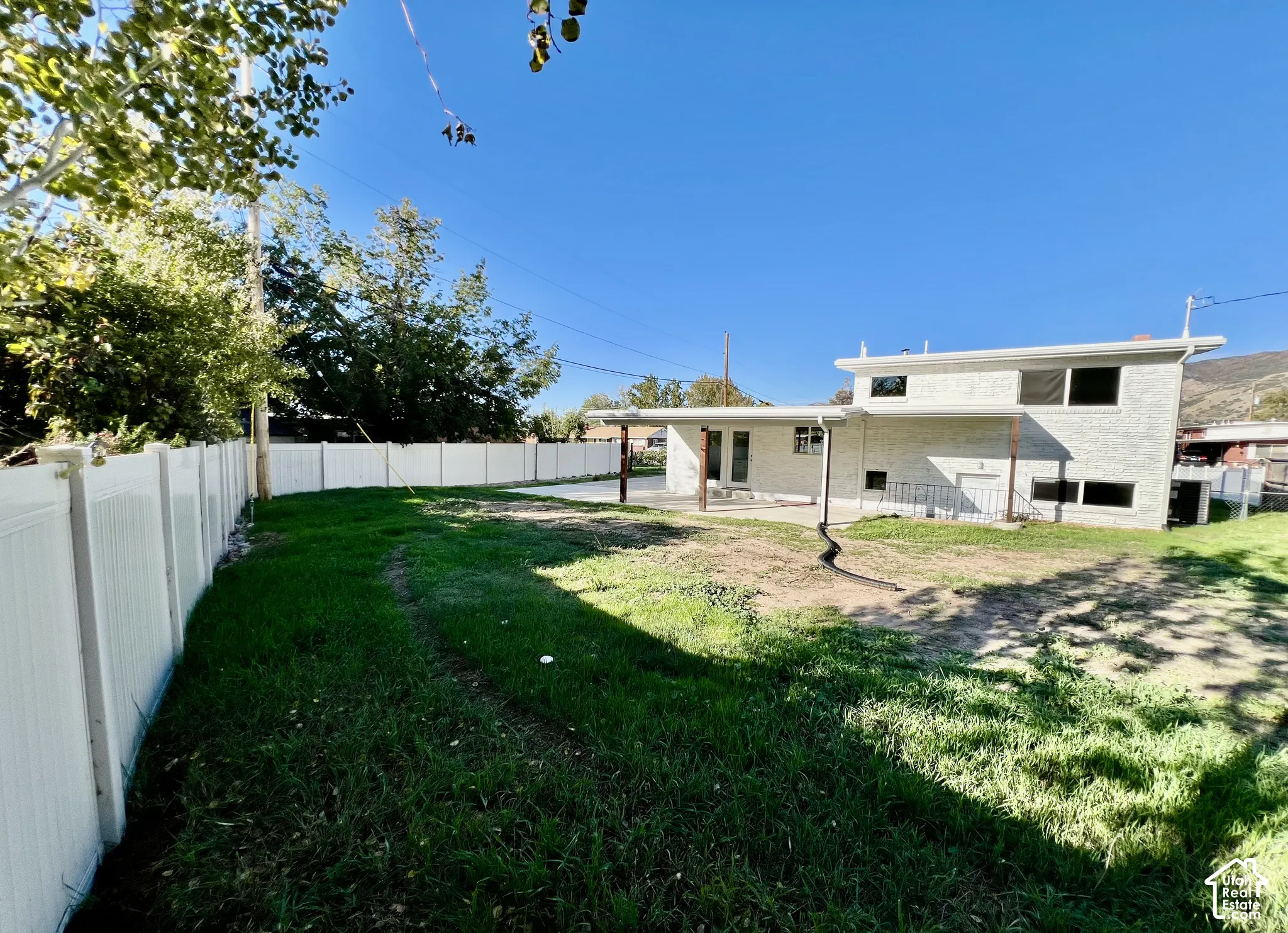 Expansive backyard with a full white privacy fence, multi-level home exterior, and a covered patio area