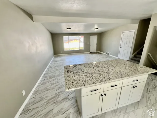 Kitchen island with a granite countertop, white cabinetry, and matte black hardware