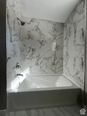 Bathtub shower combination with white and gray patterned tile surround, chrome shower head, and matching chrome fixtures