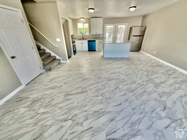 Open-concept living space with large format tile flooring, a kitchen island, stainless steel refrigerator, and dual French doors