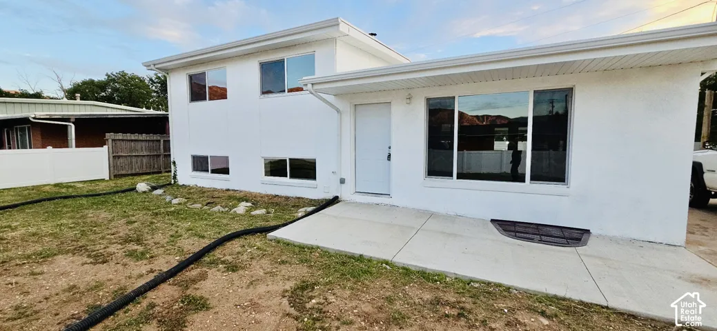 White stucco exterior with multiple windows, a concrete patio, and a white entry door