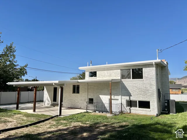White brick exterior with multiple windows, a covered patio featuring wood-toned posts, and a concrete patio