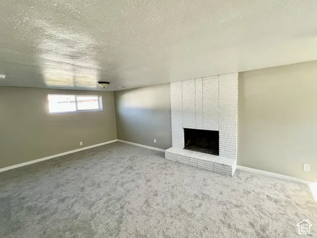 Spacious room featuring a white brick fireplace, light gray carpeting, and a window providing natural light