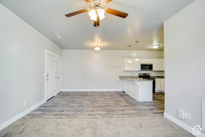 Open-concept living area with a ceiling fan, wood-finish flooring, and white kitchen cabinetry