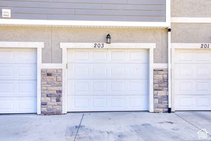 Exterior featuring multiple white panel garages, stone-clad columns, stucco finishing, and horizontal siding