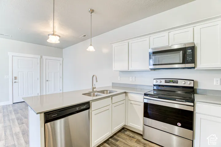 Kitchen featuring white shaker cabinetry, stainless steel appliances, light-toned countertops, and wood-finish flooring