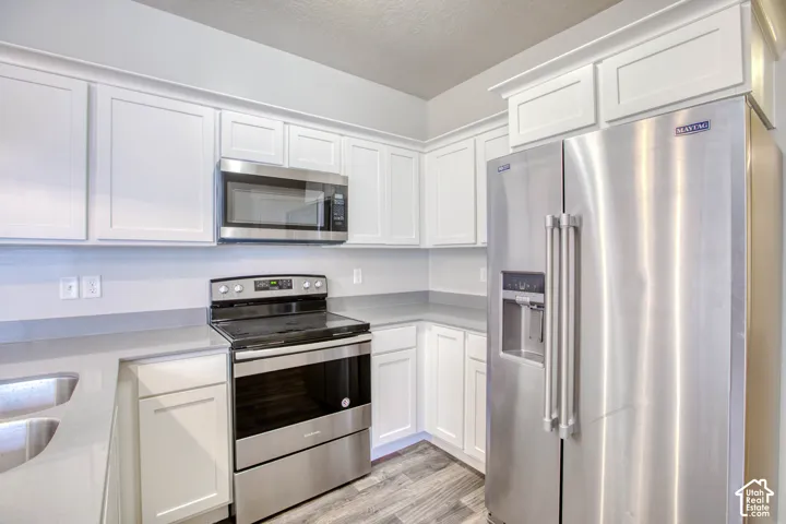 Modern kitchen featuring white shaker cabinetry, stainless steel appliances, light gray countertops, and wood-finish flooring