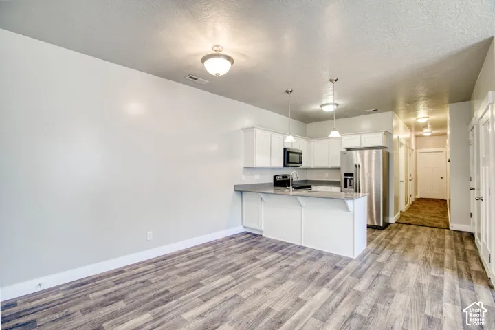 Open-concept kitchen with white cabinetry and stainless steel appliances, featuring a peninsula with countertop seating