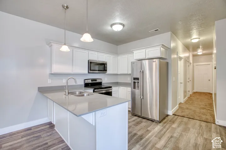 Kitchen featuring white cabinetry, gray countertops, stainless steel appliances, wood-finish flooring, and pendant lighting