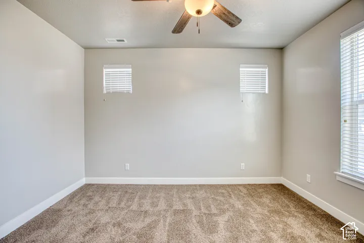 Carpeted room featuring a ceiling fan with light fixture, multiple windows with blinds, and neutral wall tones